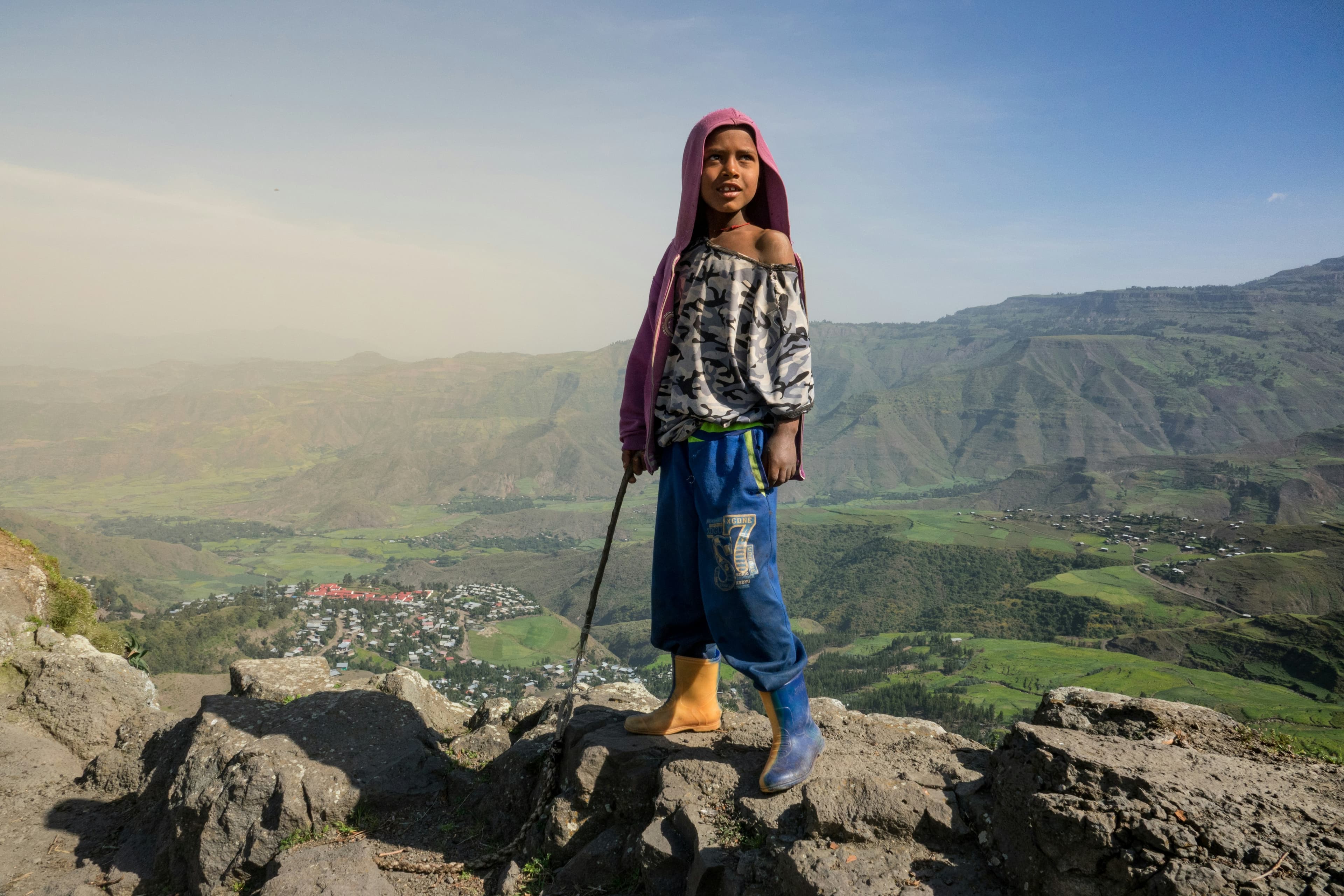 Child standing on mountain overlooking Ethiopian valley with purple hijab